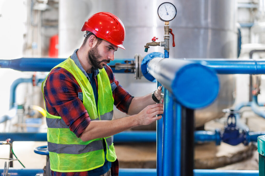 A young man is performing maintenance on the pumps at the heating plant to ensure that they are functioning properly