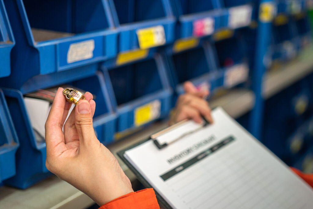 A worker's hand is holding metal ring object, a machinery spare part with blurred background of storage shelf. Industrial working scene photo, selective focus.